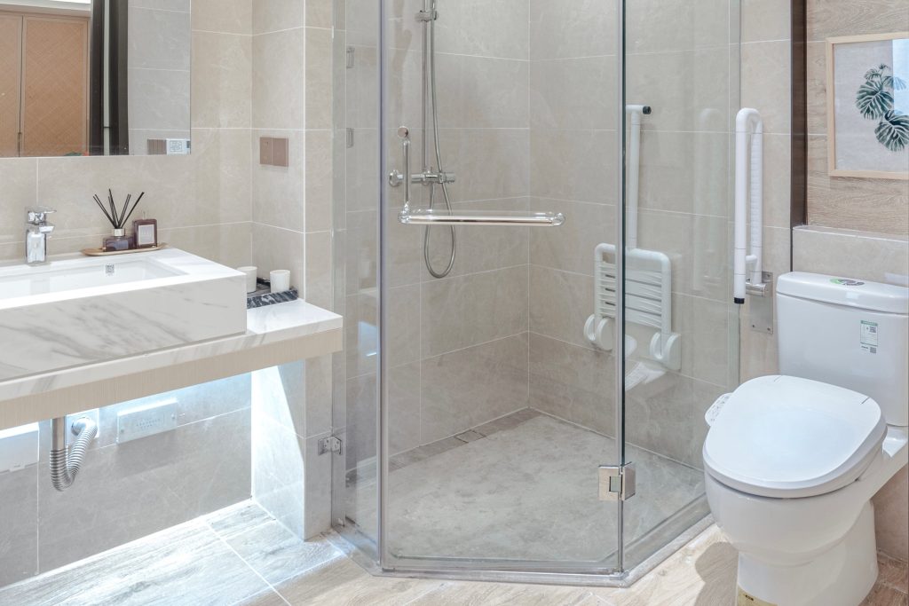 Ein helles, modernes Badezimmer mit einer bodengleichen Dusche, einem klappbaren Duschsitz an der Wand und montierten Sicherheits-Haltegriffen neben der Toilette.