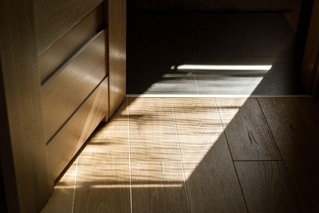 Eine geöffnete Innentür aus Holz mit einer flachen, barrierefreien Übergangsschiene auf dem Fußboden als Beispiel für Schwellenentfernung im Haus.