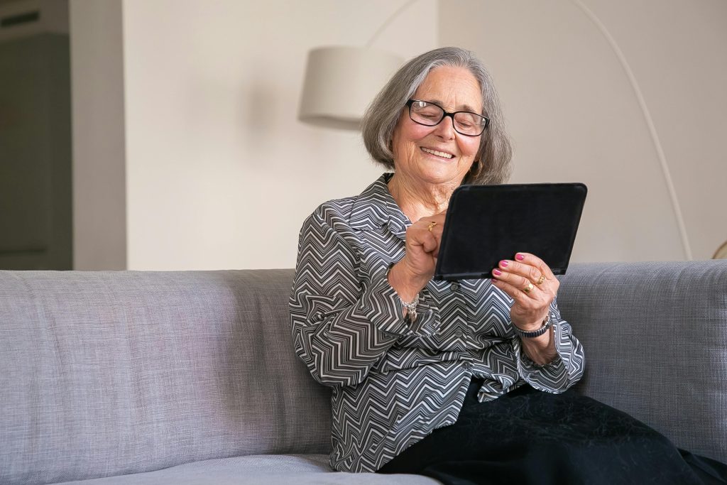 Seniorin informiert sich erleichtert auf dem Tablet über zustehende Pflegehilfsmittel.