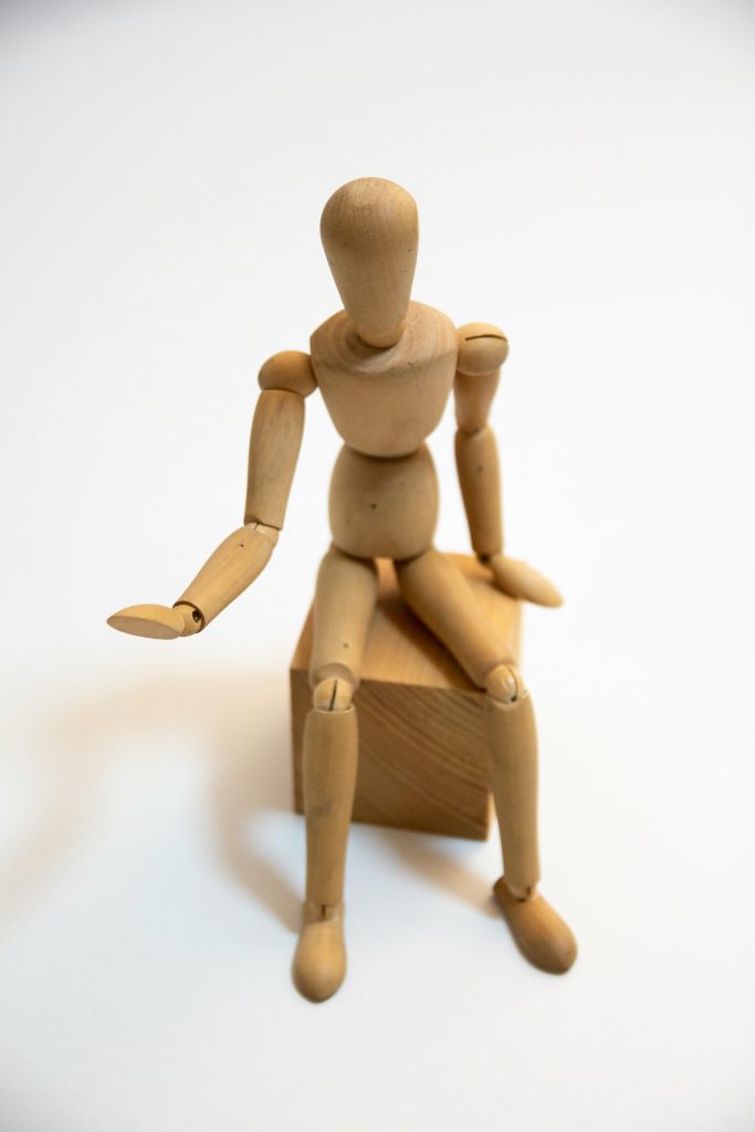 Eine sitzende Gliederpuppe aus Holz streckt hilfesuchend eine Hand aus als symbolische Darstellung für erste körperliche Einschränkungen und den Anspruch auf Pflegegrad 1.