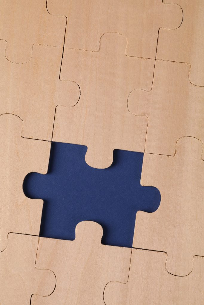 Ein unvollständiges Holzpuzzle mit einer auffälligen Lücke auf blauem Untergrund als Symbol für Gedächtnisverlust und Demenzerkrankungen.