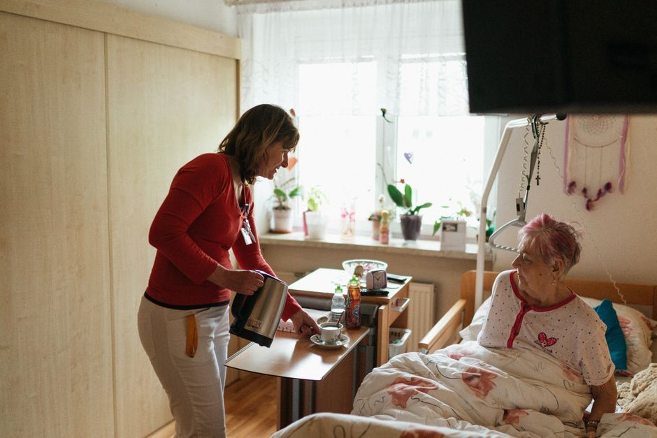 pflegerin bringt tee seniorin bett zuhause häusliche pflege schlafzimmer