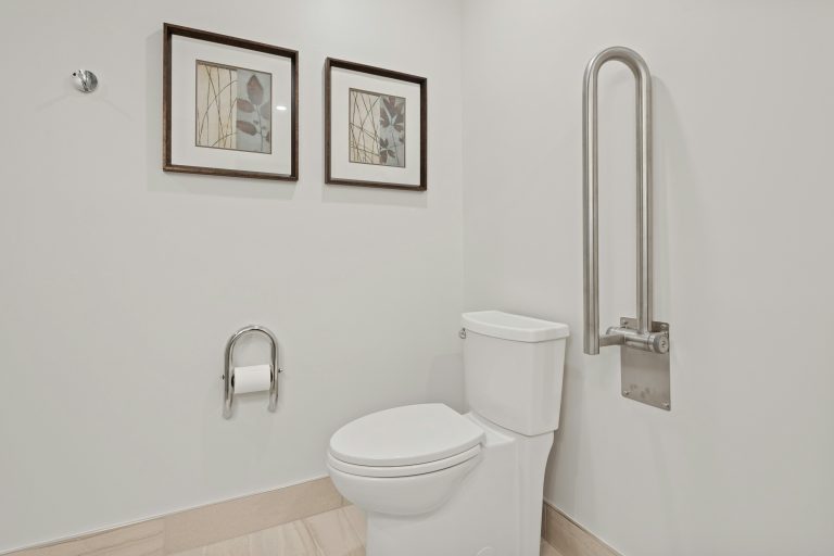 Ein barrierefreies Badezimmer mit einer weißen Toilette und einem stabilen Stützklappgriff aus Edelstahl an der Wand als Beispiel für den pflegegerechten Umbau einer Wohnung.