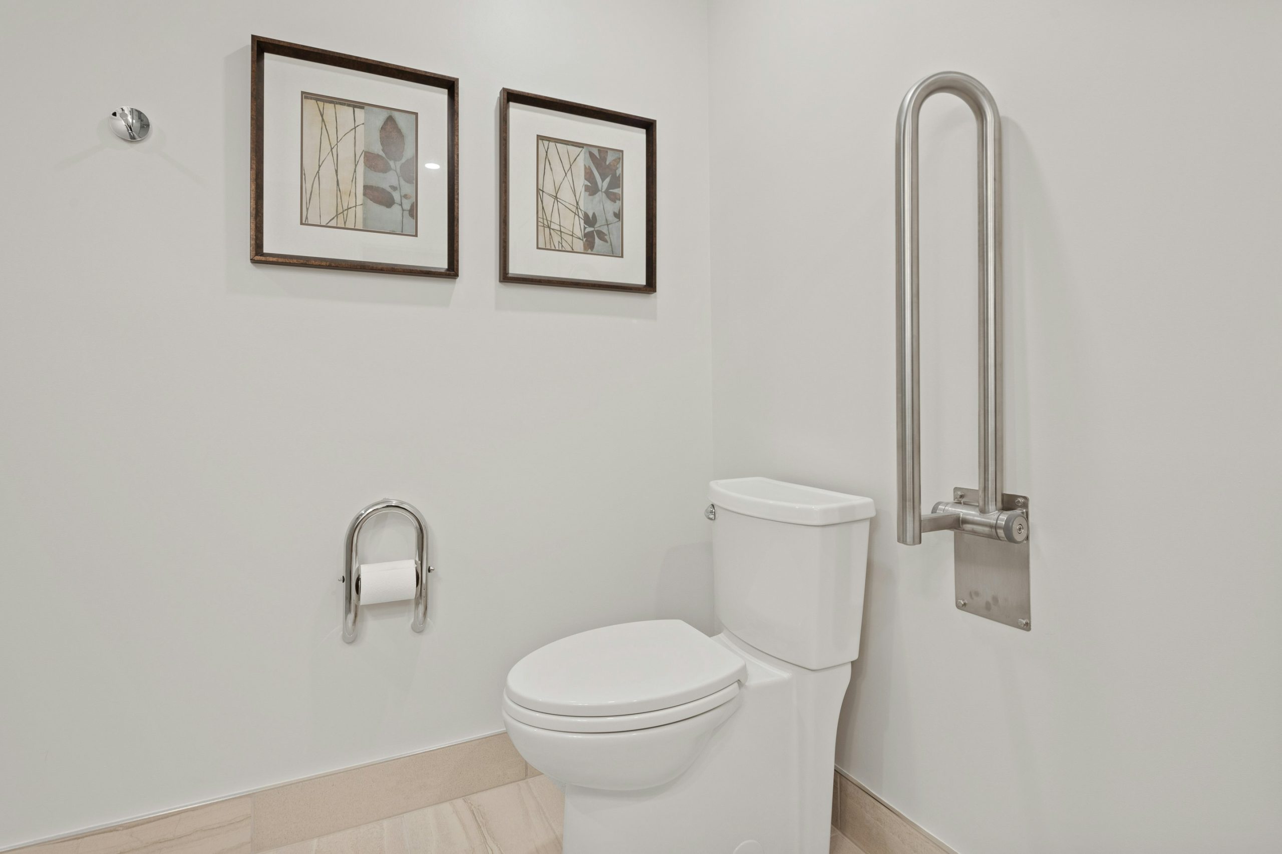 Ein barrierefreies Badezimmer mit einer weißen Toilette und einem stabilen Stützklappgriff aus Edelstahl an der Wand als Beispiel für den pflegegerechten Umbau einer Wohnung.